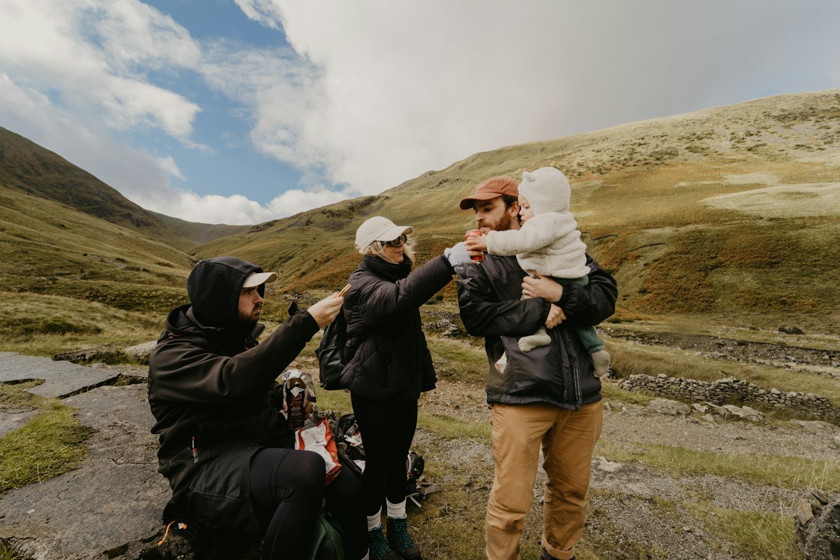 O familie cu un copil mic împărtășind o băutură împreună în drumeție la munte