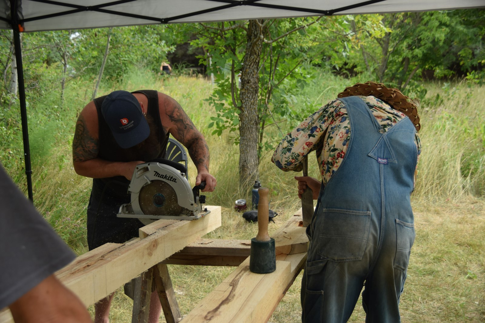 Two people building a wooden structure with tools outdoors
