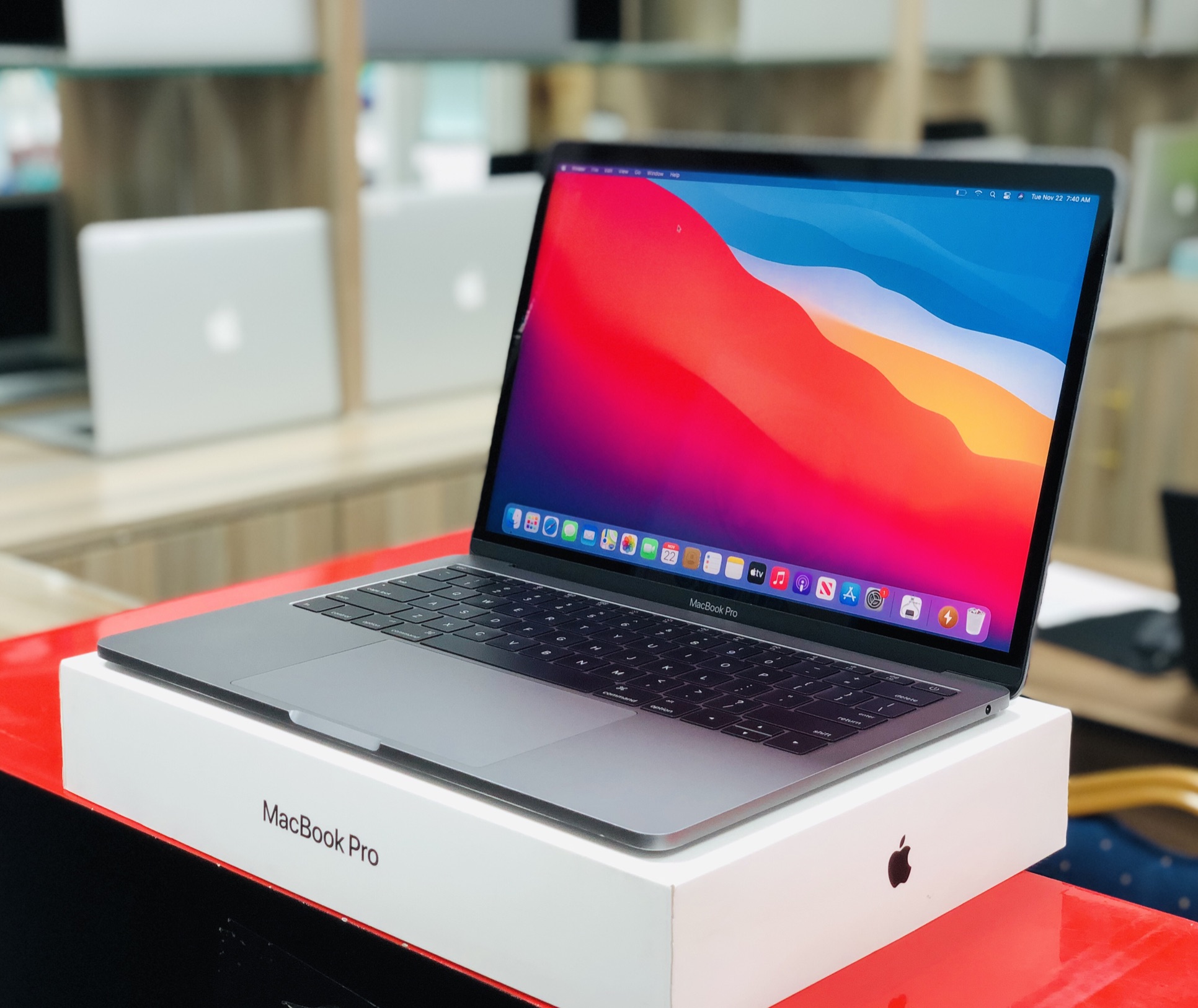 A space gray MacBook Pro 2019 with Touch Bar, open and powered on, resting on its retail box